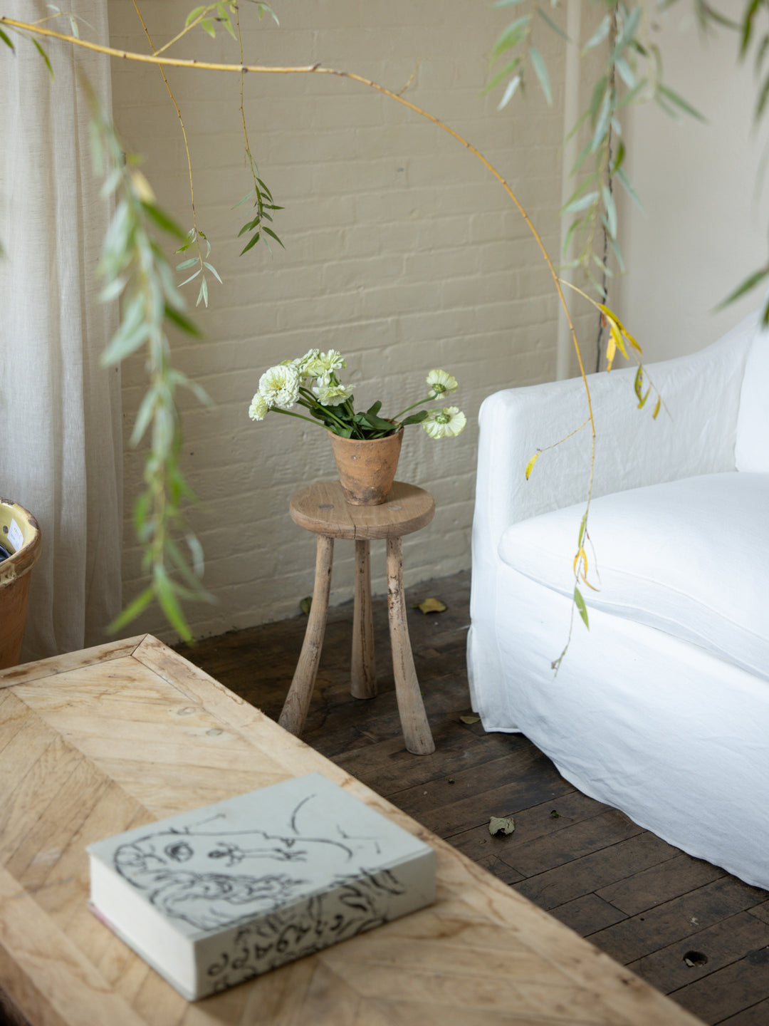 a vase of flowers sits on le curved leg tripod stool next to a couch