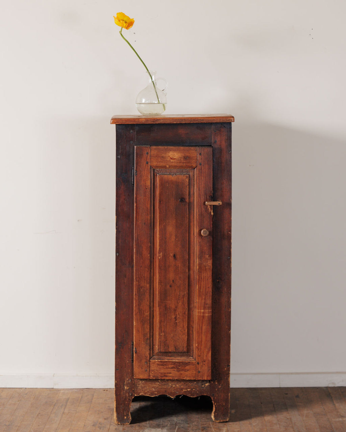 Rustic wooden cabinet with a yellow flower in a vase on top.