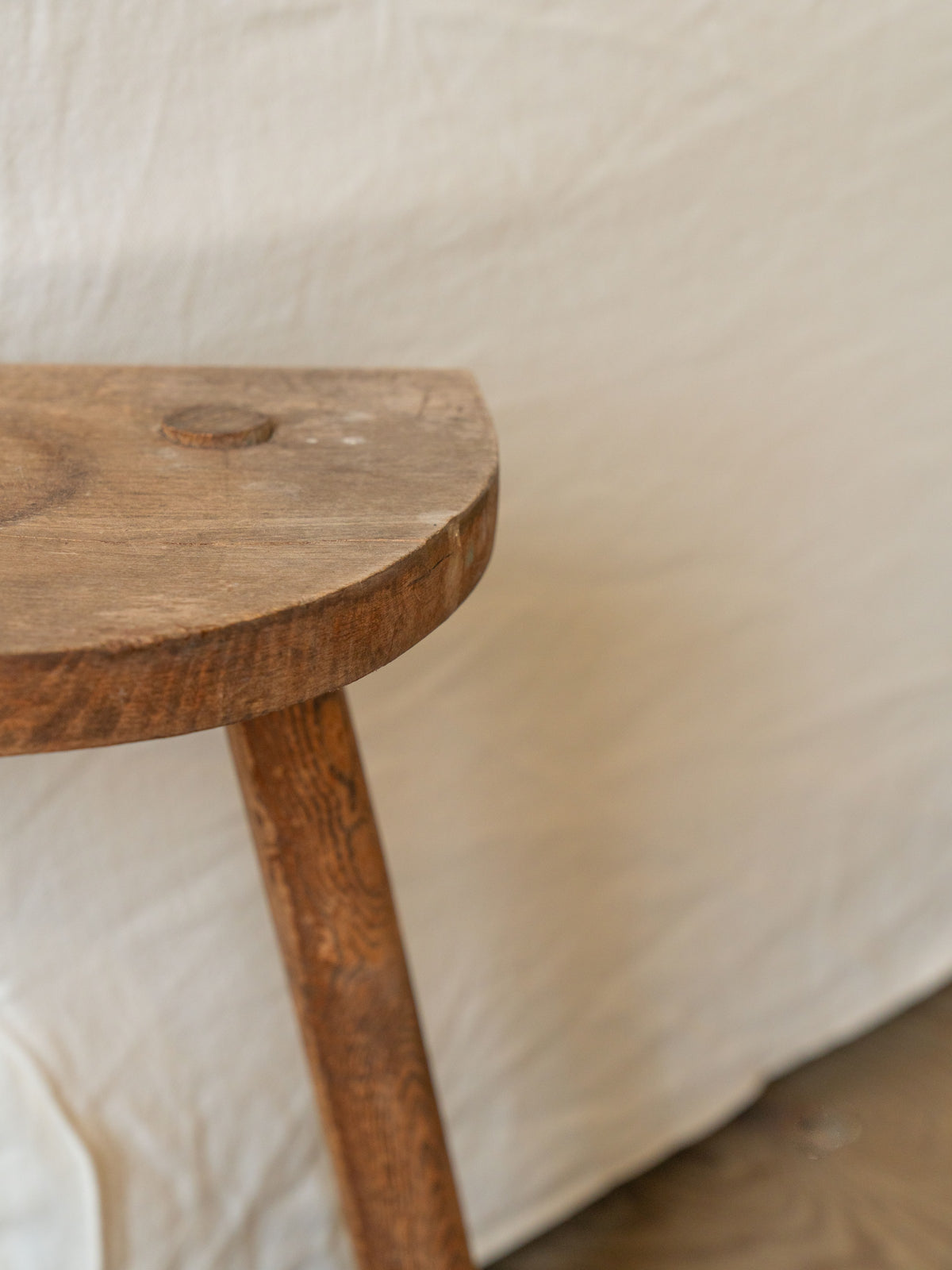 a wooden stool is sitting on a wooden floor in front of a white cloth .