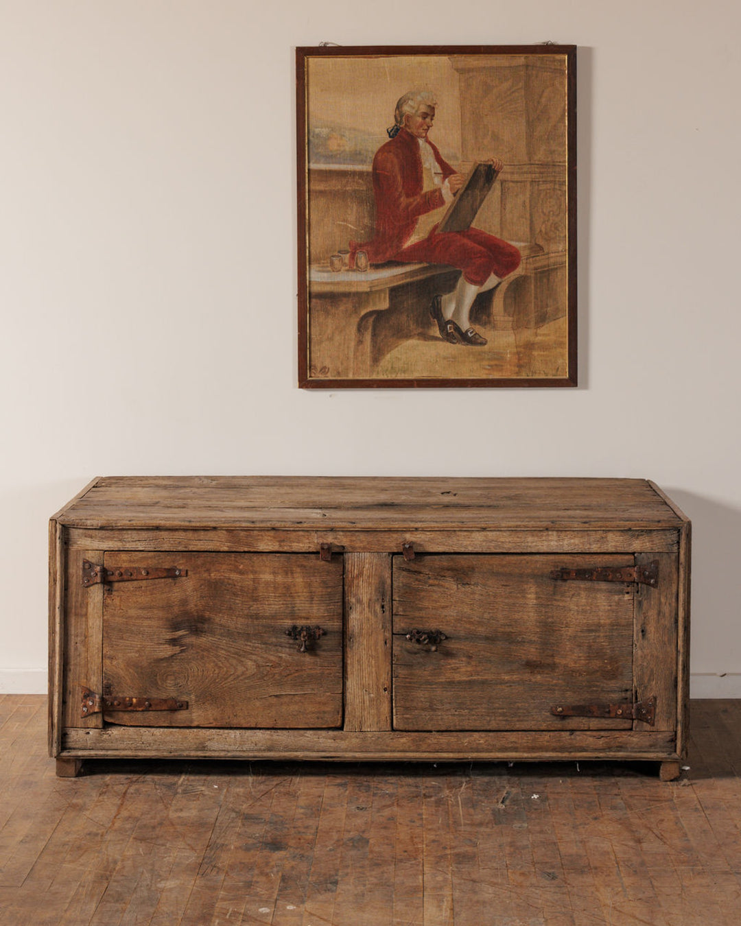 A rustic two-door wooden cabinet below a framed painting of a man in a red jacket.