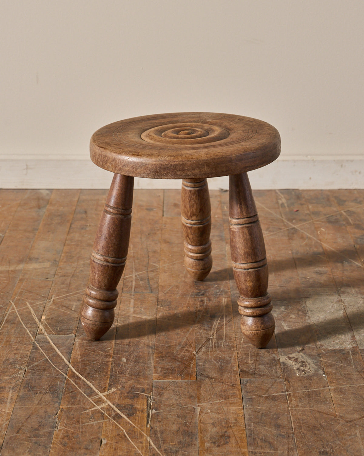 A rustic three-legged wooden stool with a round seat featuring concentric carved grooves.
