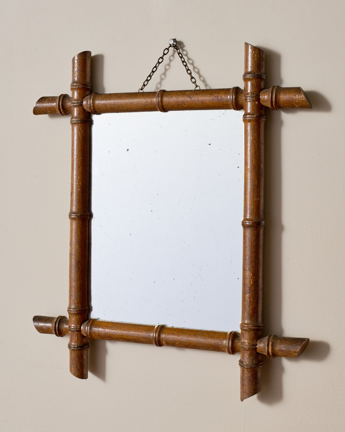 A square mirror with a light brown bamboo frame hanging on a beige wall.