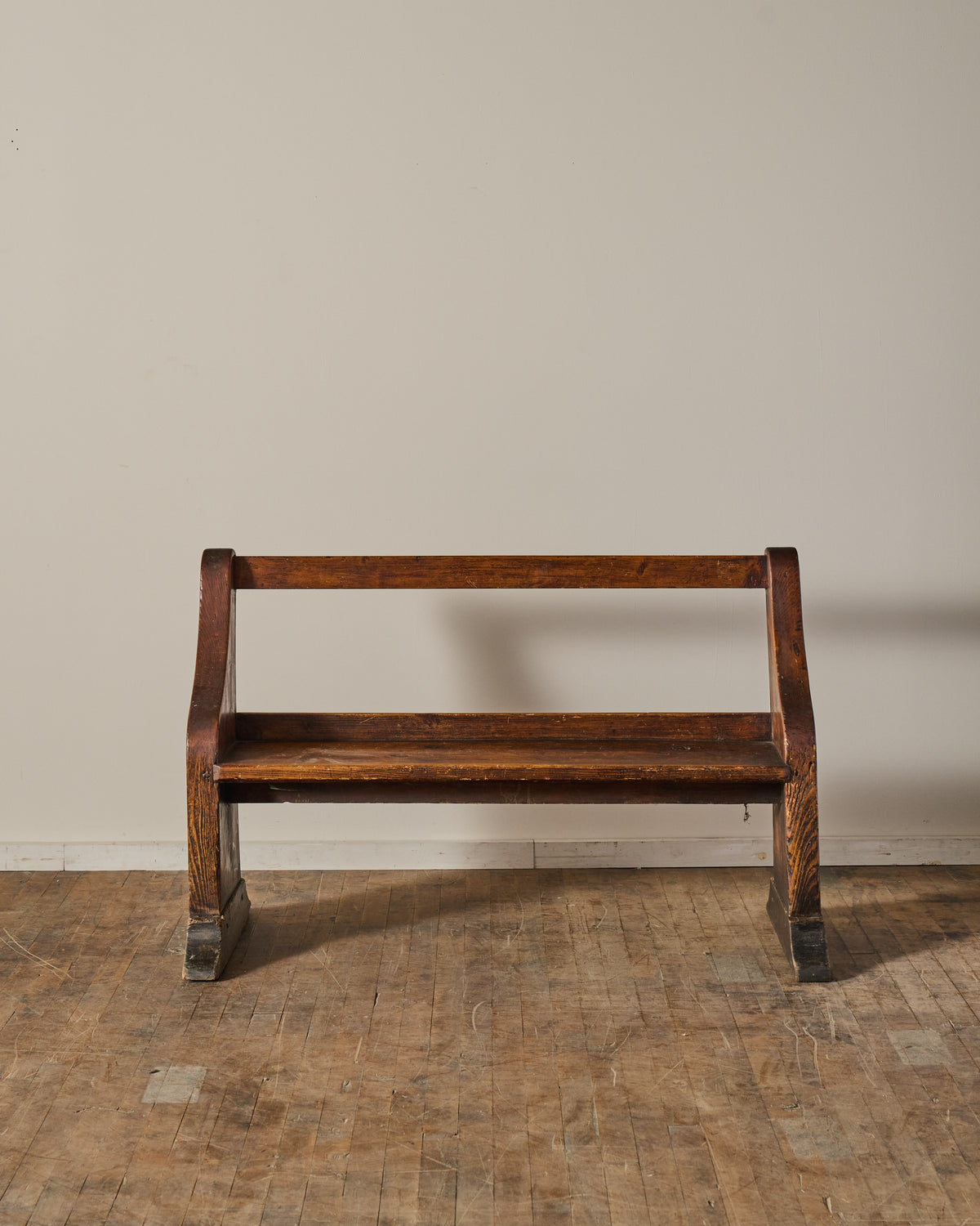 A dark brown wooden bench on a worn plank floor against a light wall.