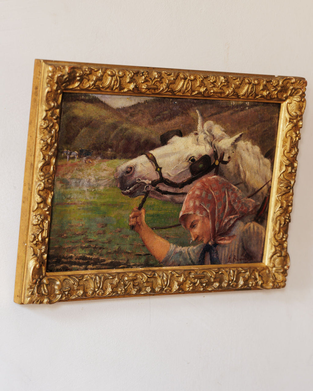 A painting in an ornate golden frame of a woman in a headscarf leading two white horses in a tilled field.