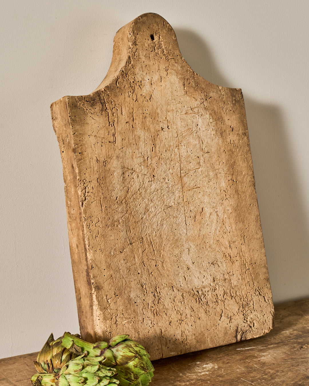 Rustic wooden cutting board with a curved top and hole, an artichoke below it.