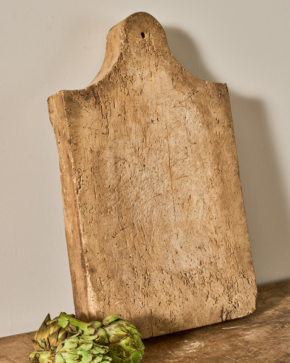 Rustic wooden cutting board with a curved top and hole, an artichoke below it.