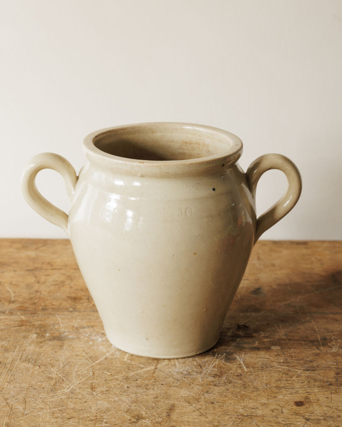 A vintage cream stoneware pot with two handles, marked '10', on a wooden surface.