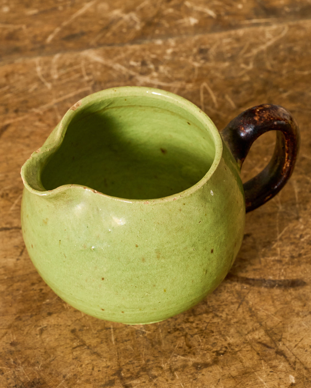 A light green ceramic creamer with a dark brown handle on a wooden surface.