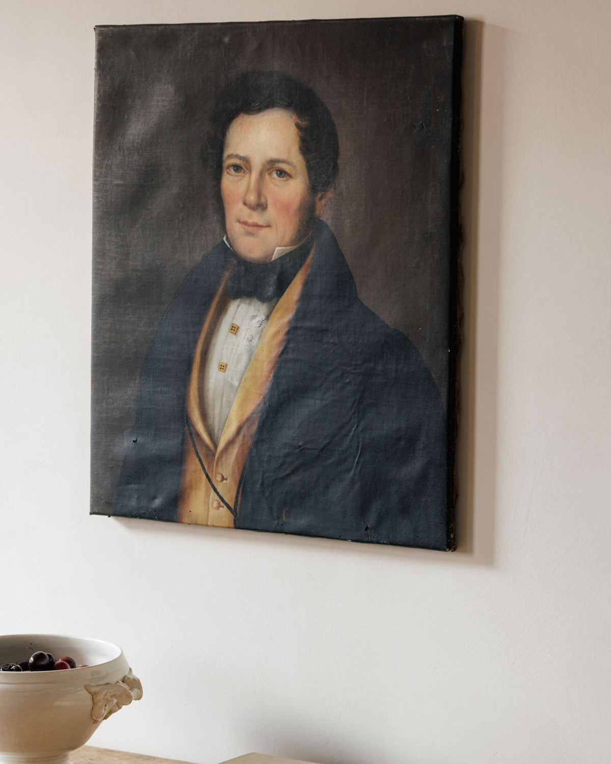 Antique portrait of a man in a dark coat and yellow vest on a light wall.